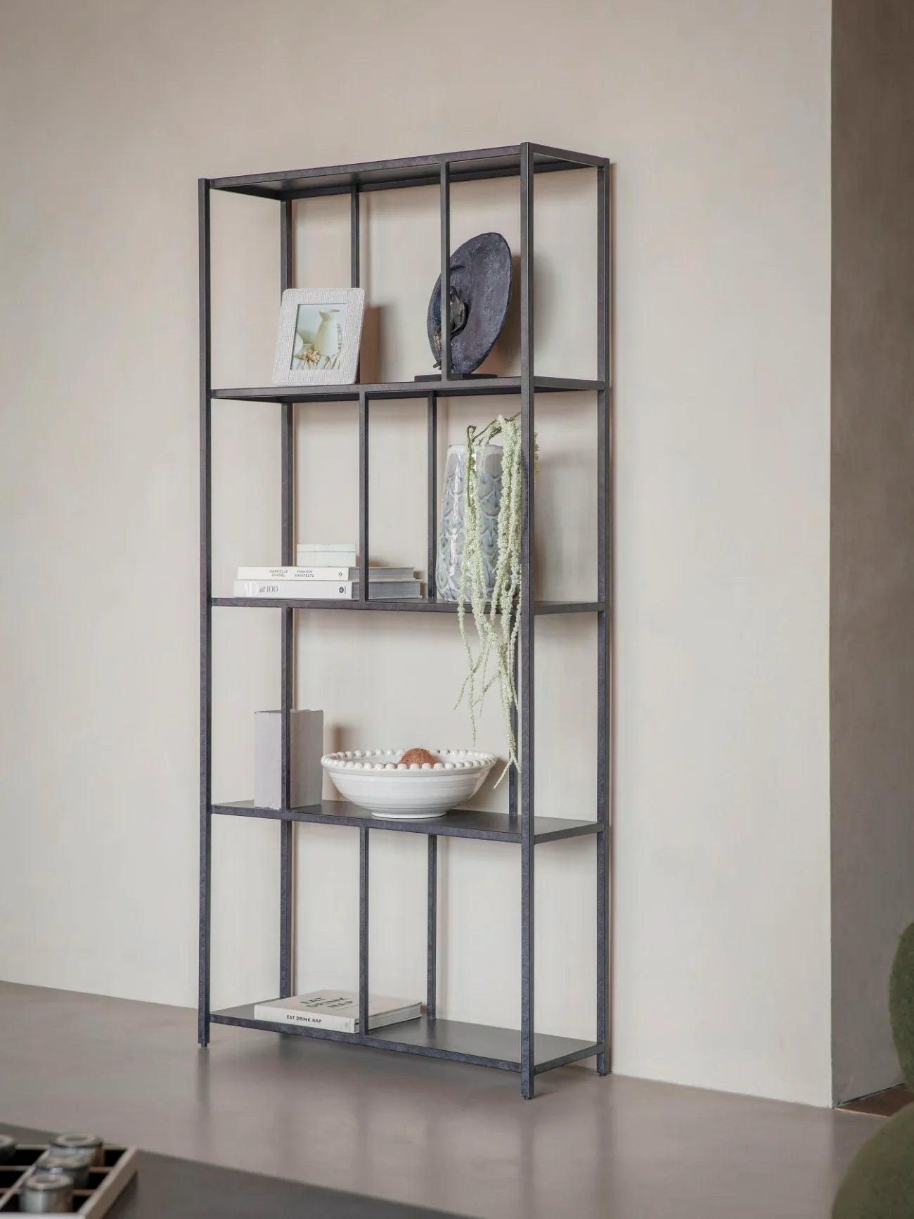 Mottled black metal shelving unit with decor items against a beige wall.