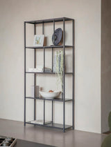 Mottled black metal shelving unit with decor items against a beige wall.