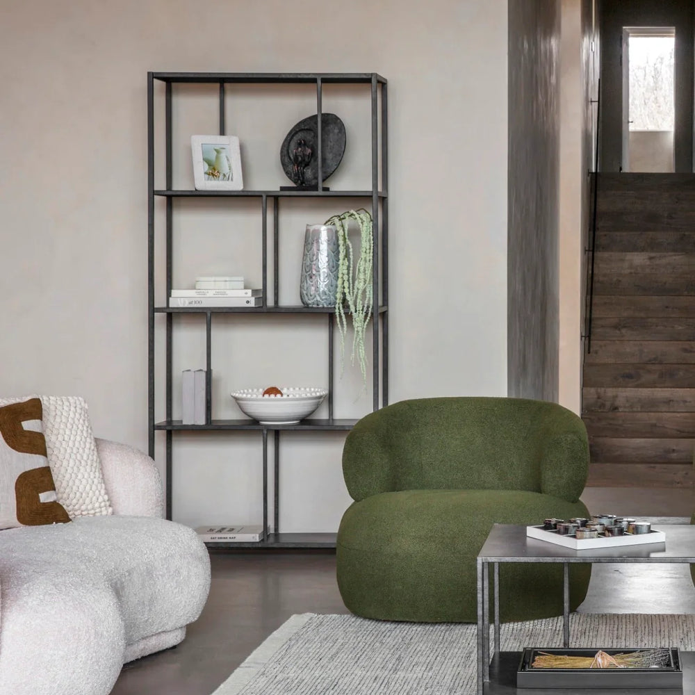 Black metal shelving unit in modern living room with green chair and decor items.