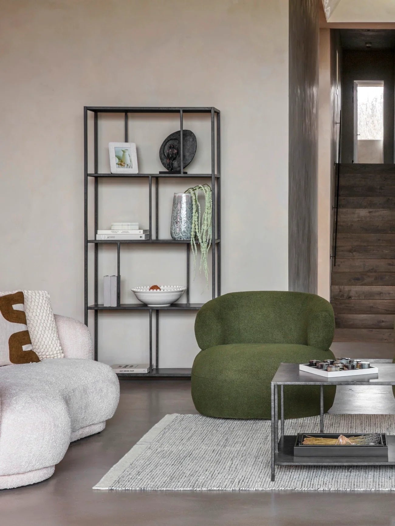 Black metal shelving unit in modern living room with green chair and decor items.