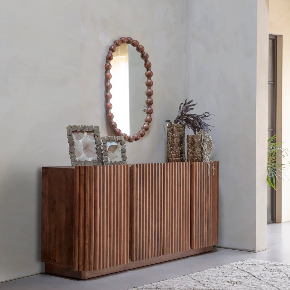 Wooden sideboard with ribbed doors in a modern hallway, adorned with decor items.