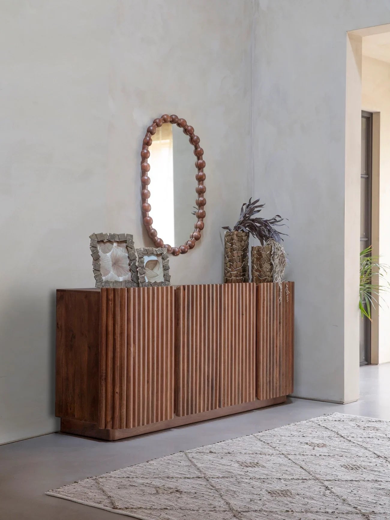 Wooden sideboard with ribbed doors in a modern hallway, adorned with decor items.