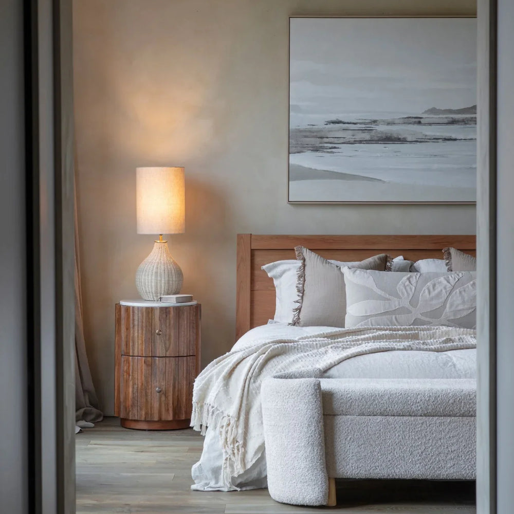 Curved wooden bedside with marble top in cozy bedroom setting.