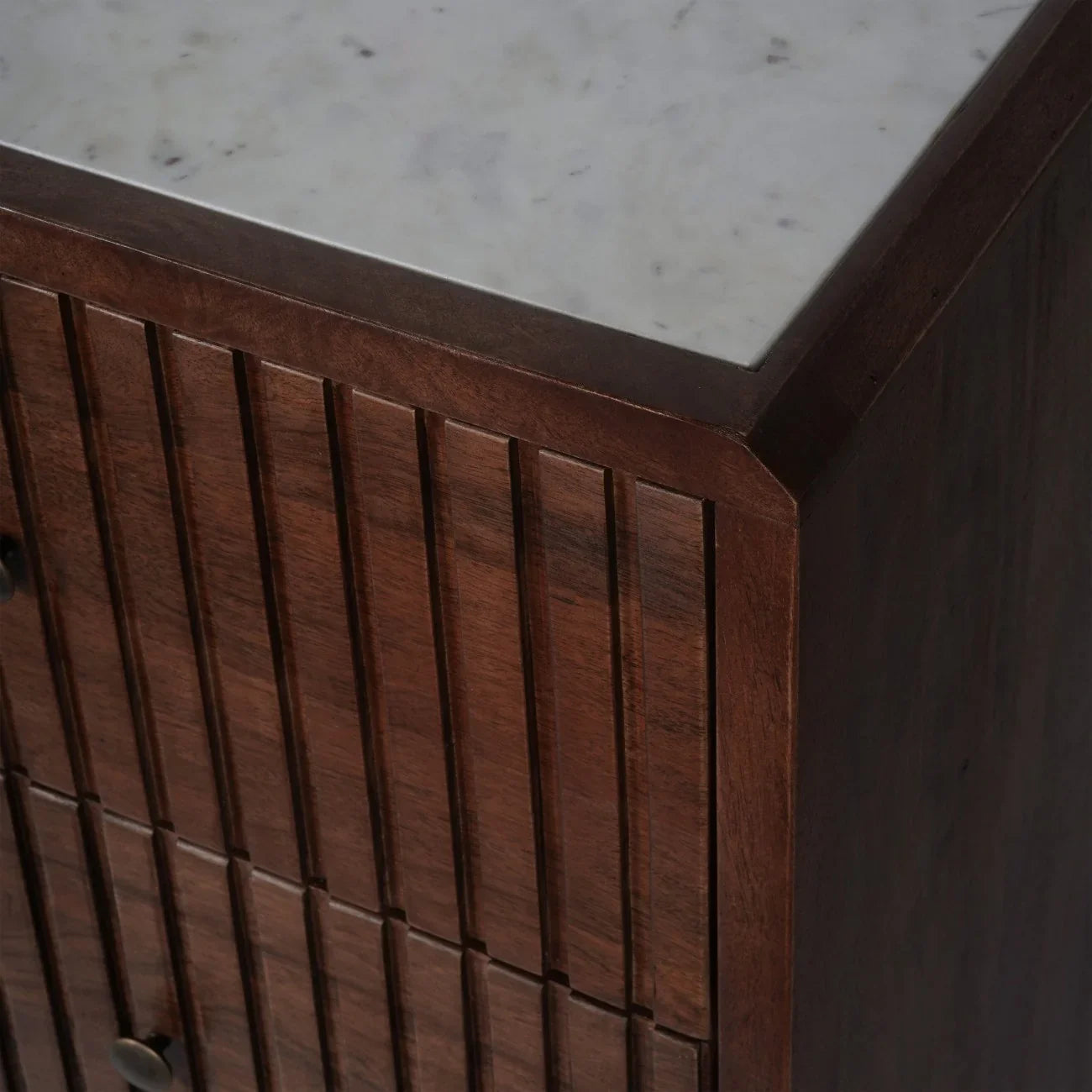Dark wood chest corner with vertical grooves and smooth marble top.