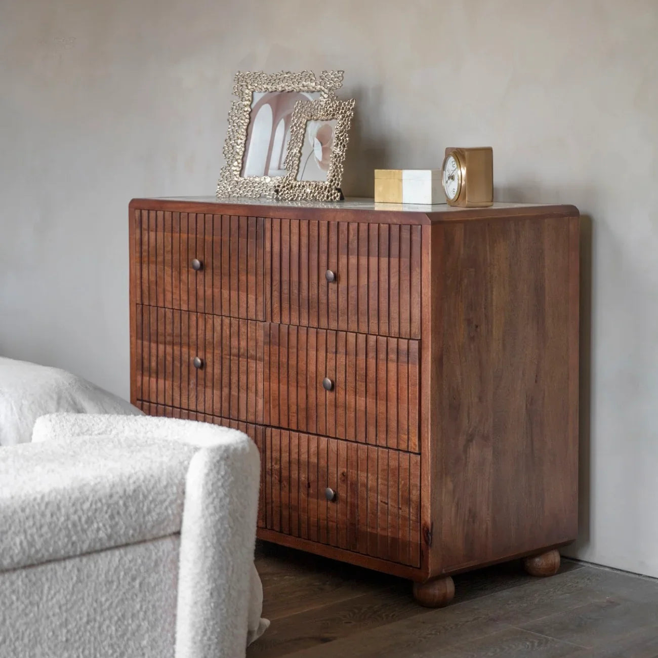 Wooden drawer chest with marble top, adorned with decorative frames and a clock.