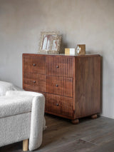 Wooden drawer chest with marble top, adorned with decorative frames and a clock.
