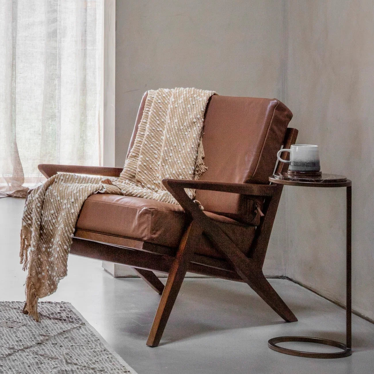 Brown leather armchair with wooden frame, draped with a beige throw.