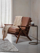 Brown leather armchair with wooden frame, draped with a beige throw.