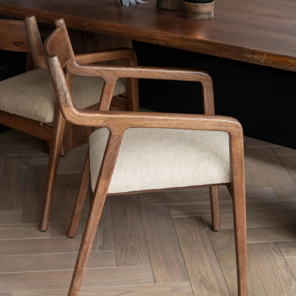 Beige upholstered chair with wooden frame beside a dark wood table.