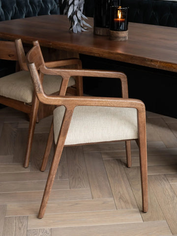 Beige upholstered chair with wooden frame beside a dark wood table.