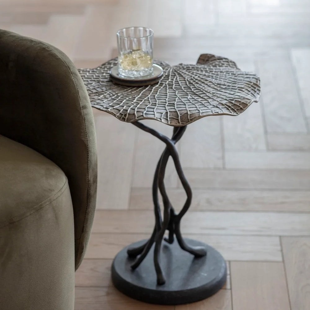 Cast aluminium leaf-shaped table beside a green sofa on wooden flooring.