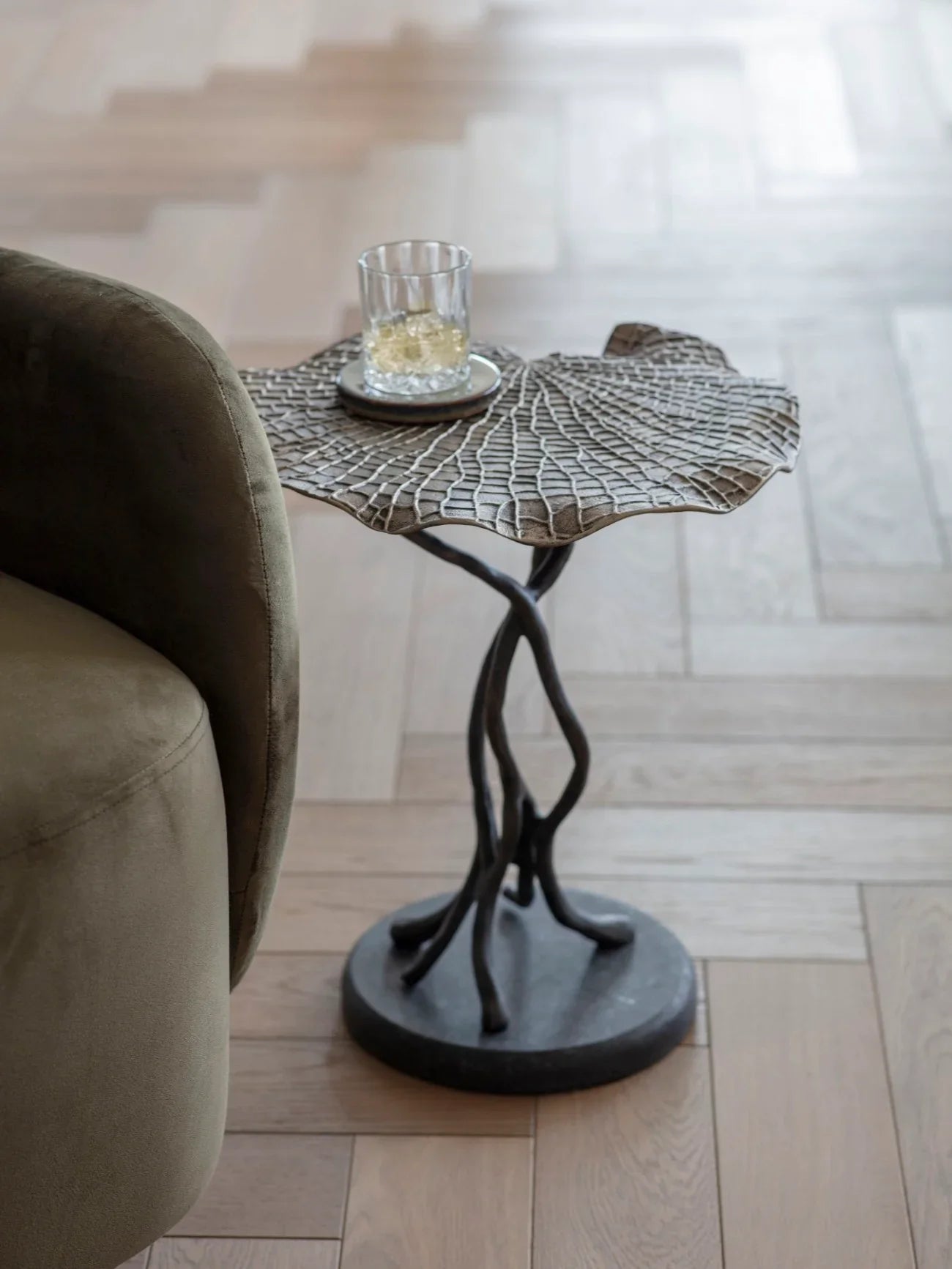 Cast aluminium leaf-shaped table beside a green sofa on wooden flooring.