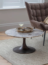 Round quartz coffee table with dark base in cozy living room setting.