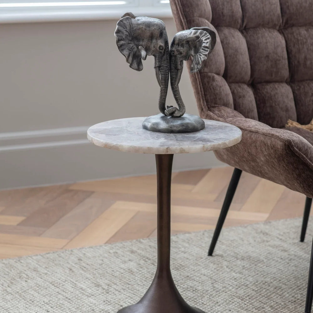 Marble-topped side table with elephant sculpture beside a plush brown chair.