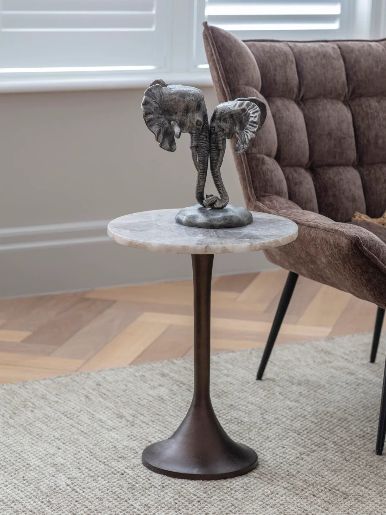 Marble-topped side table with elephant sculpture beside a plush brown chair.