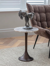 Marble-topped side table with elephant sculpture beside a plush brown chair.