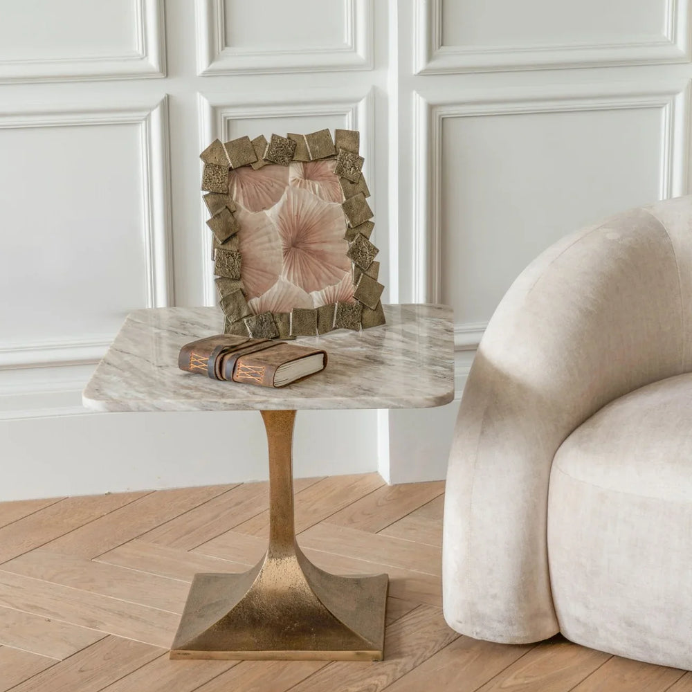Marble side table with brass base beside a beige sofa and decorative frame.