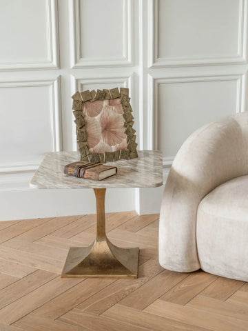 Marble side table with brass base beside a beige sofa and decorative frame.