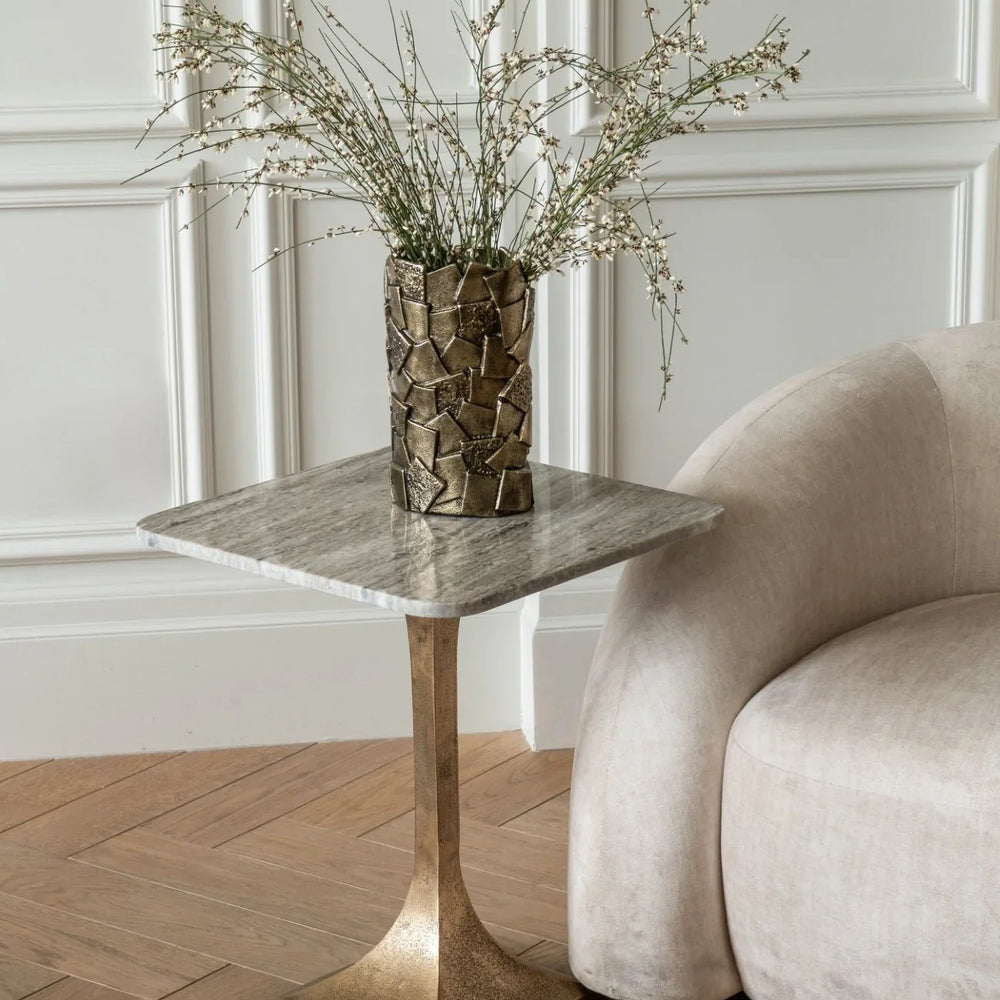 Marble side table with gold base beside cream sofa in elegant room.