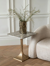 Marble side table with gold base beside cream sofa in elegant room.