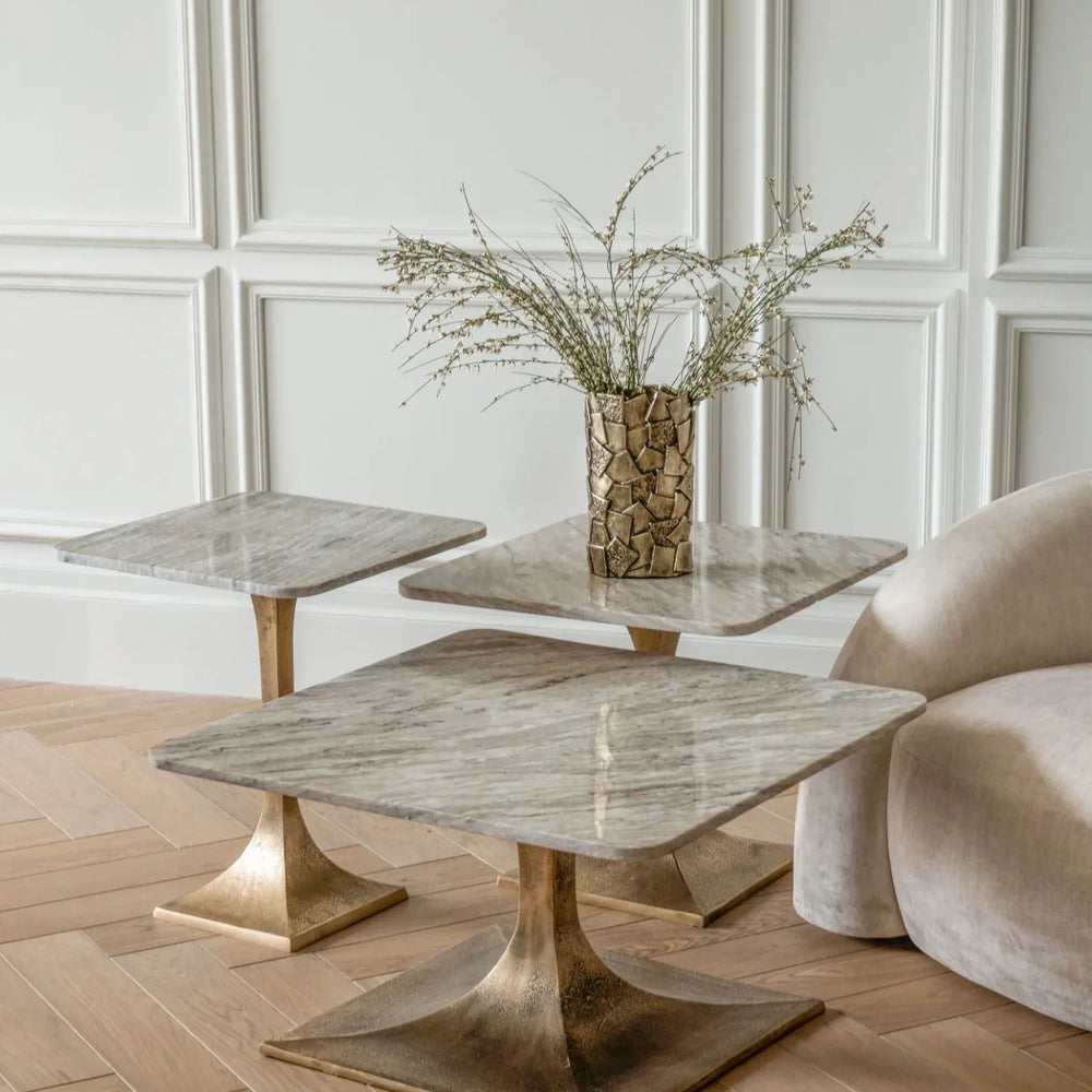 Marble side tables with bronze bases in elegant room with vase and plush chair.
