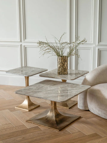 Marble side tables with bronze bases in elegant room with vase and plush chair.