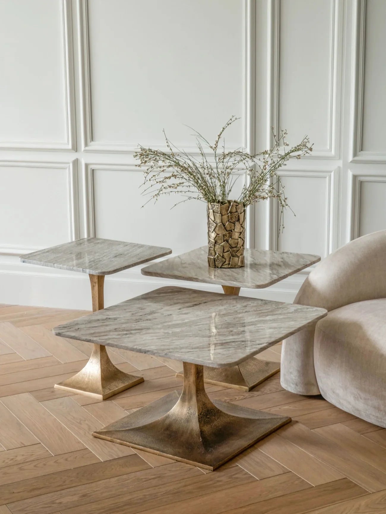 Marble side tables with bronze bases in elegant room with vase and plush chair.