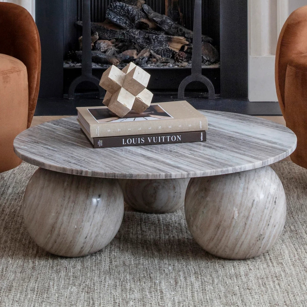 Round marble coffee table with spherical legs in front of a fireplace.