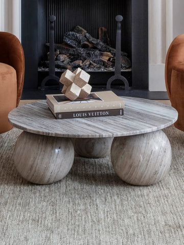Round marble coffee table with spherical legs in front of a fireplace.