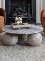 Round marble coffee table with spherical legs in front of a fireplace.