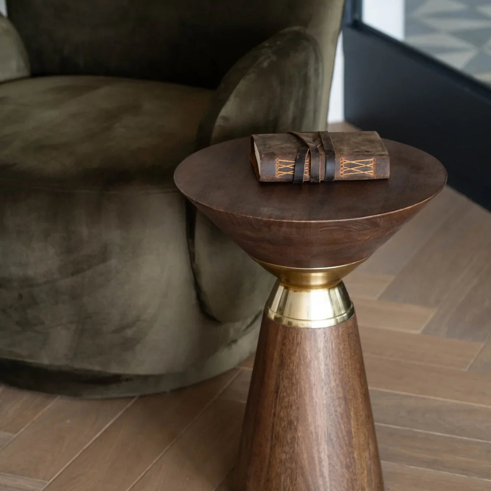 Wooden side table with brass accent next to an olive armchair on wooden floor.