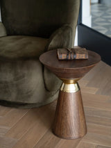 Wooden side table with brass accent next to an olive armchair on wooden floor.