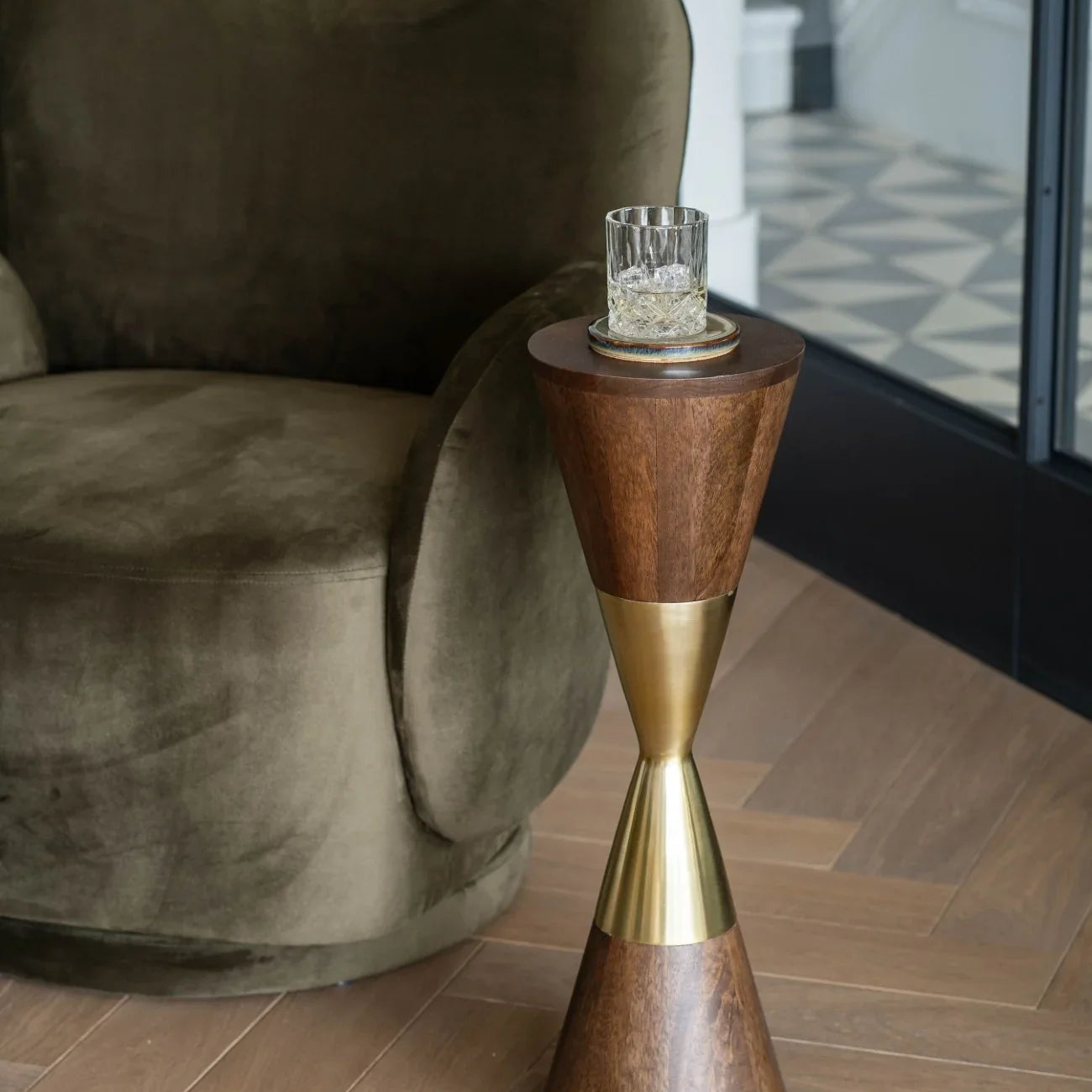 Wooden cocktail table with brass accents beside a plush olive armchair.