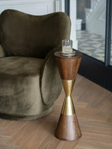 Wooden cocktail table with brass accents beside a plush olive armchair.