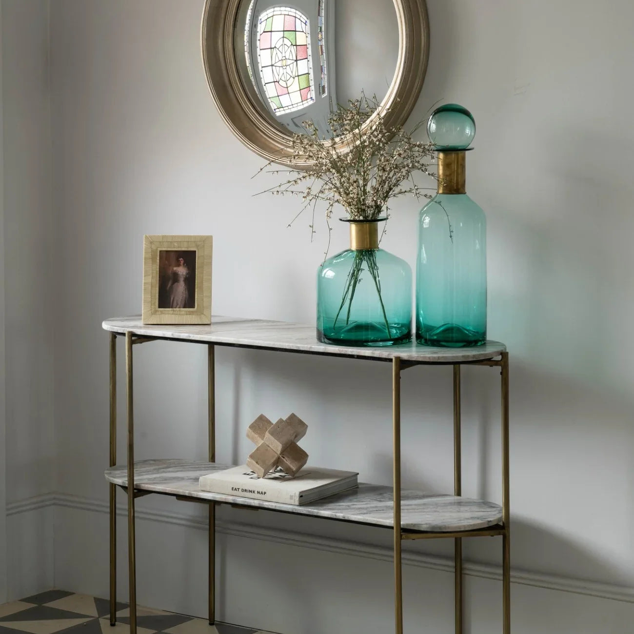 Console table with marble top in hallway, styled with teal vases and round mirror.