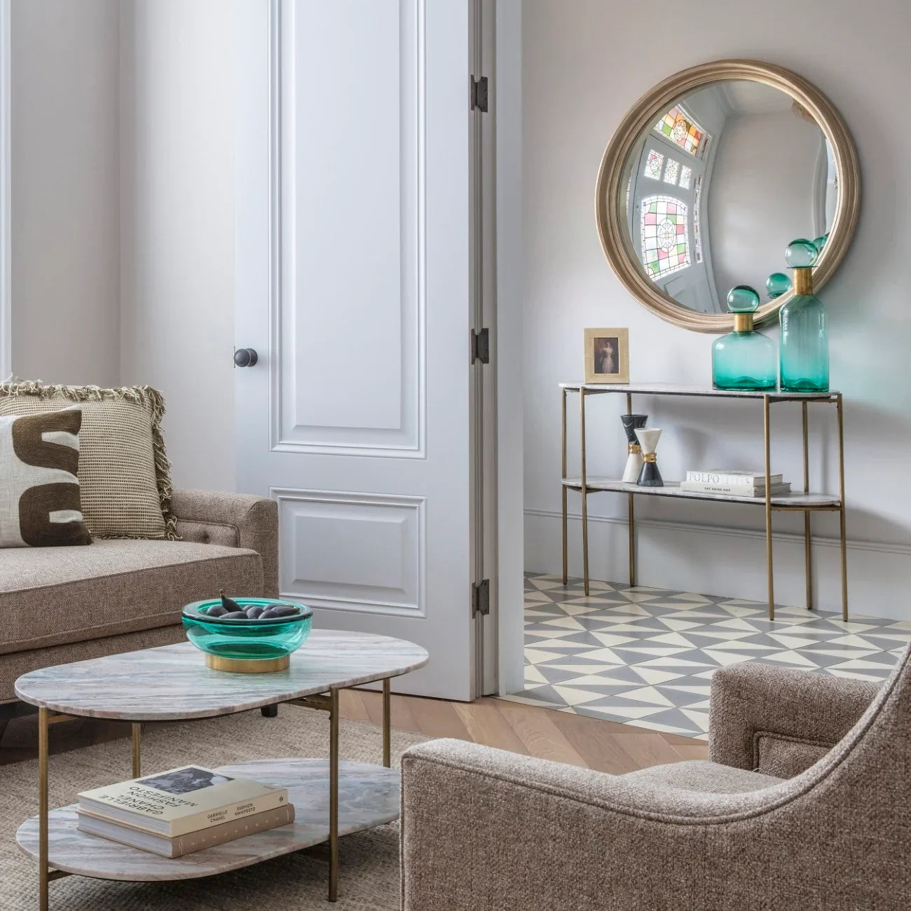 Console table with marble top in elegant room, teal vases and round mirror above.