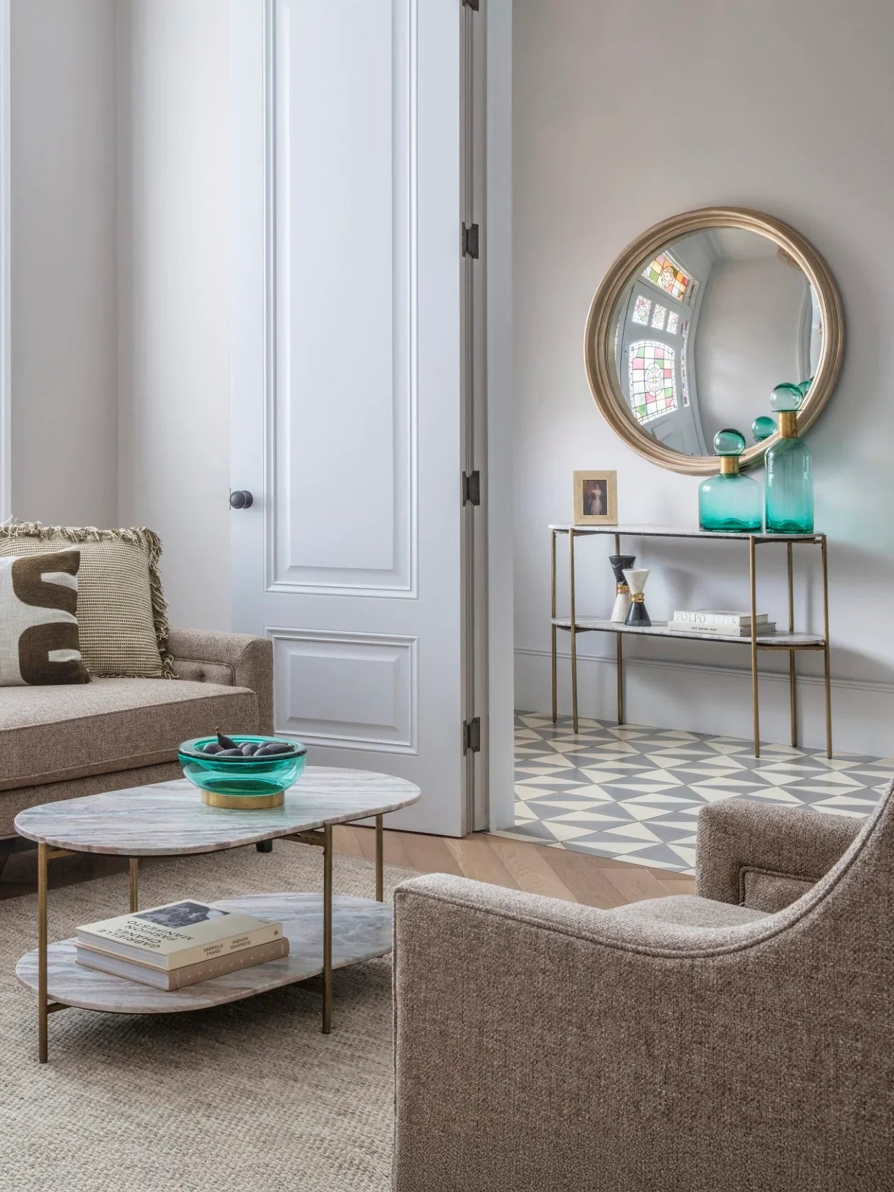 Console table with marble top in elegant room, teal vases and round mirror above.