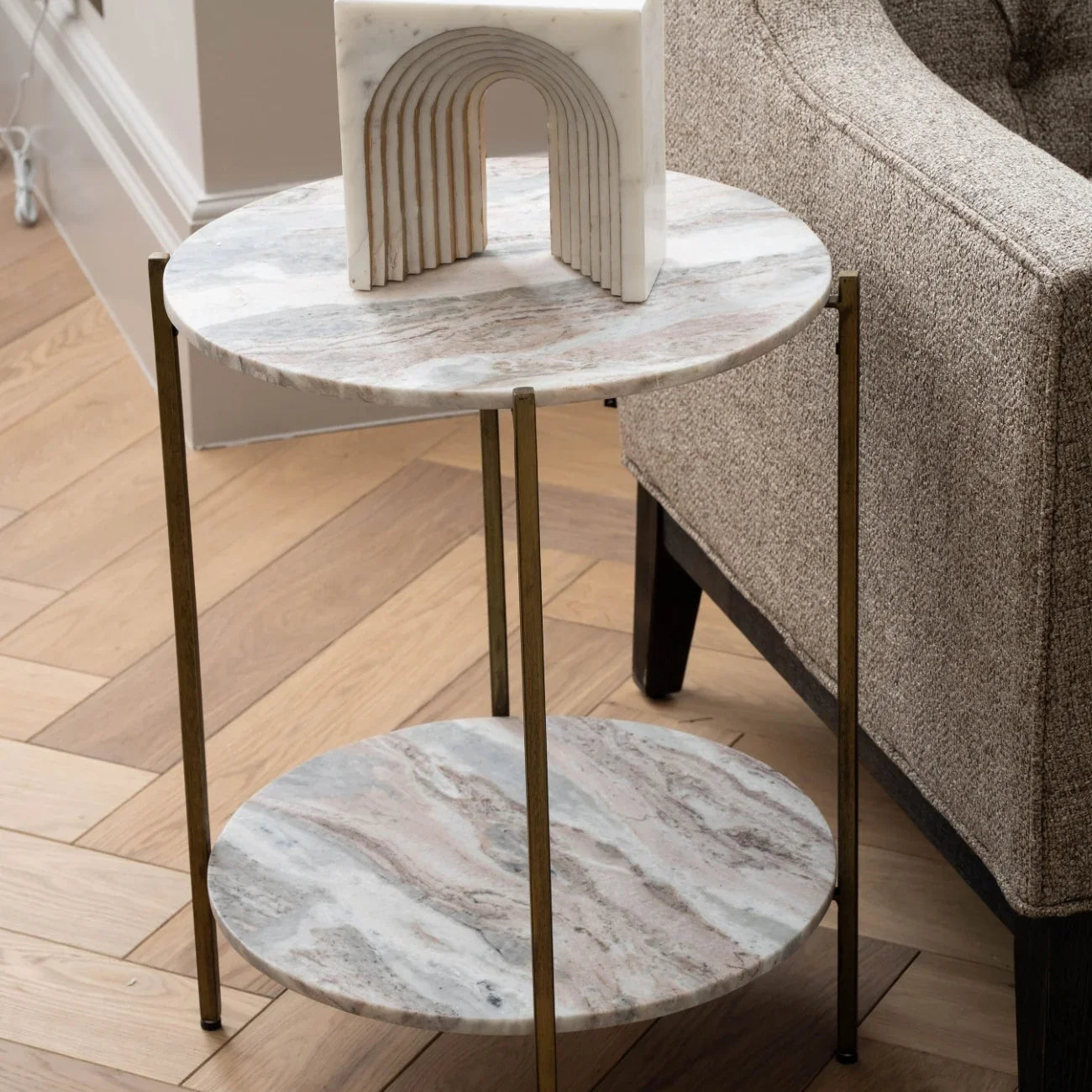 Round marble side table with brass legs beside a textured armchair.