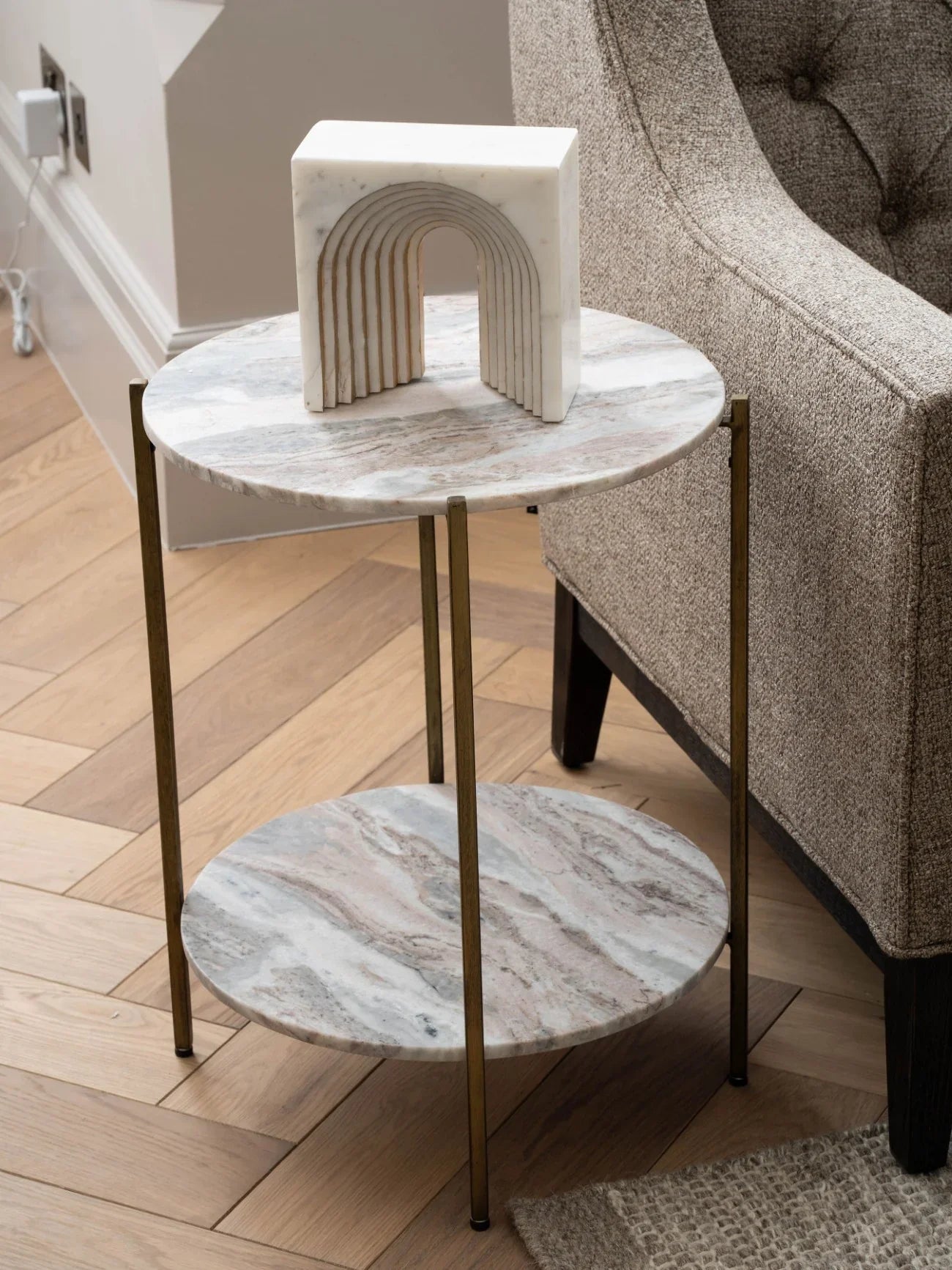 Round marble side table with brass legs beside a textured armchair.