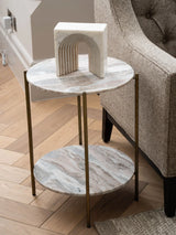 Round marble side table with brass legs beside a textured armchair.