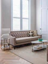 Modern side table in a cozy living room with a beige sofa and large windows.