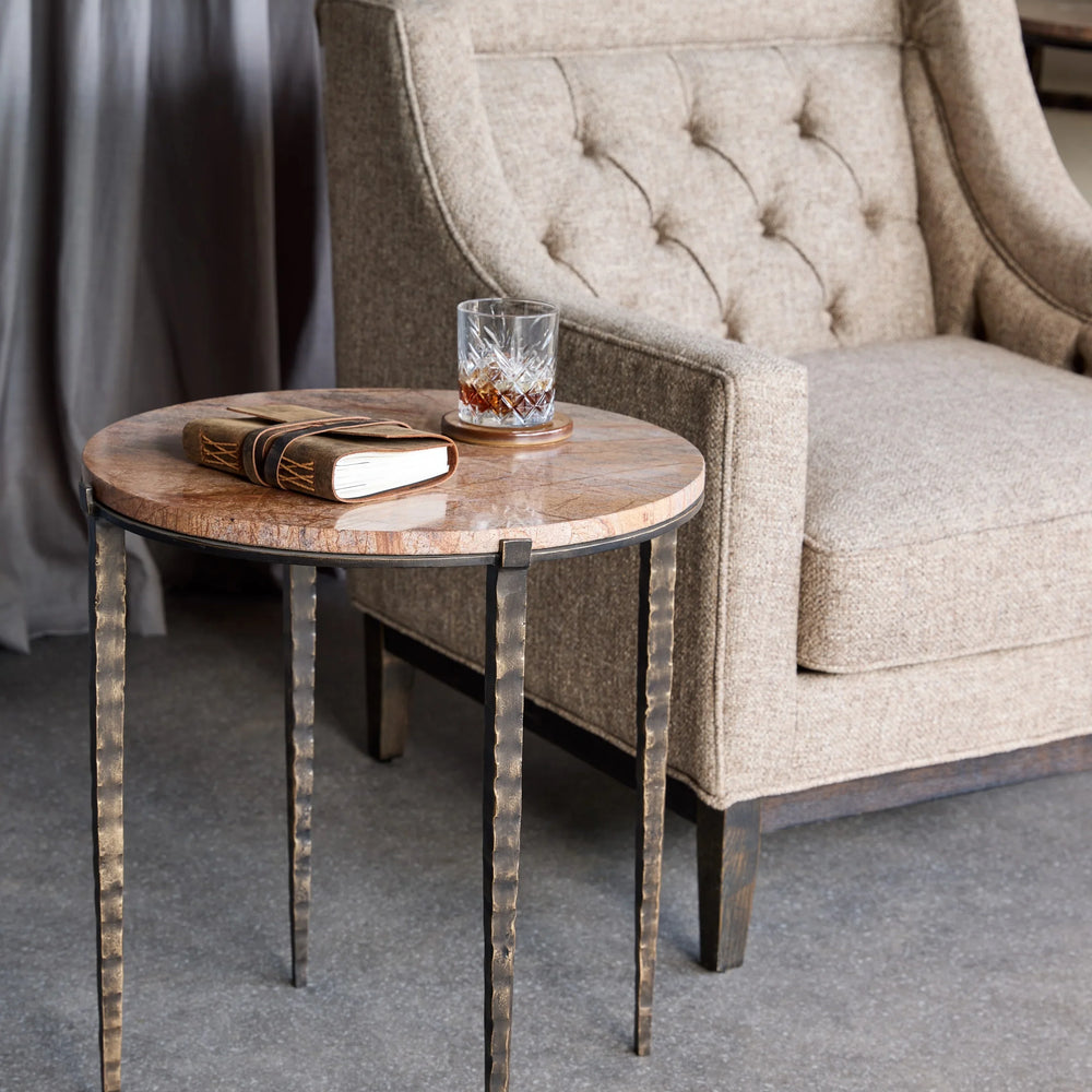 Brown marble side table beside tufted beige armchair in cozy living room setting.