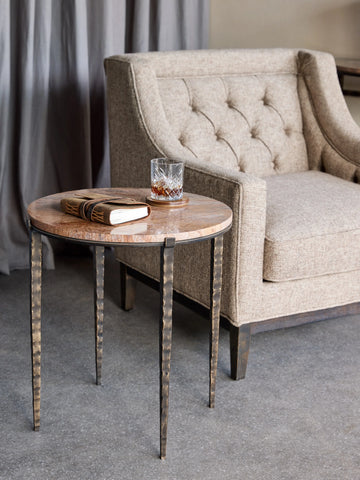 Brown marble side table beside tufted beige armchair in cozy living room setting.