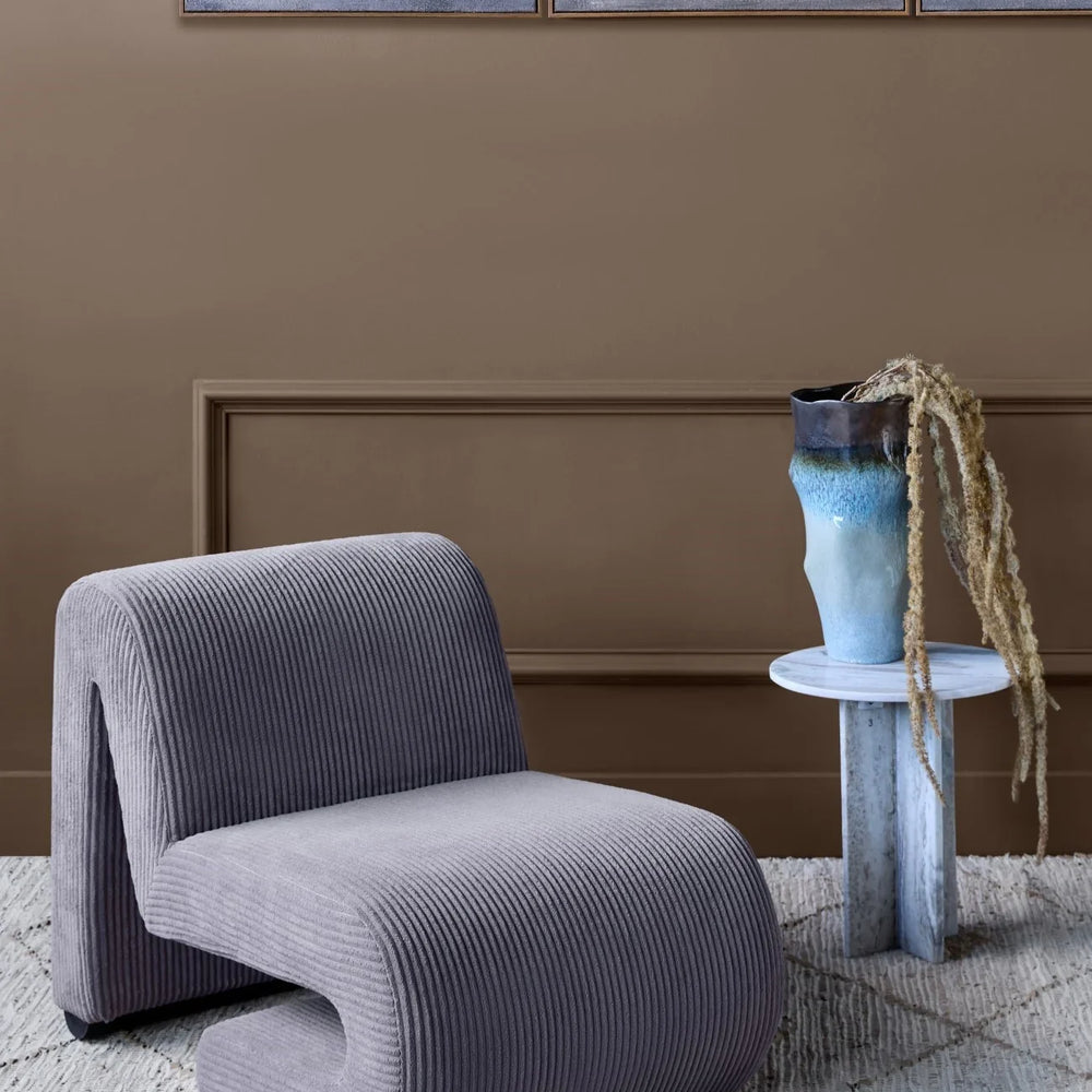 Corduroy chair in a cozy room with a side table and abstract wall art.