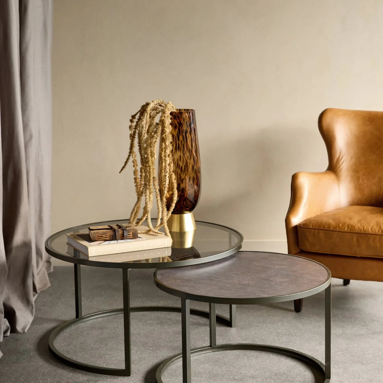 Glass and metal nesting tables in a cozy living room with leather chair.