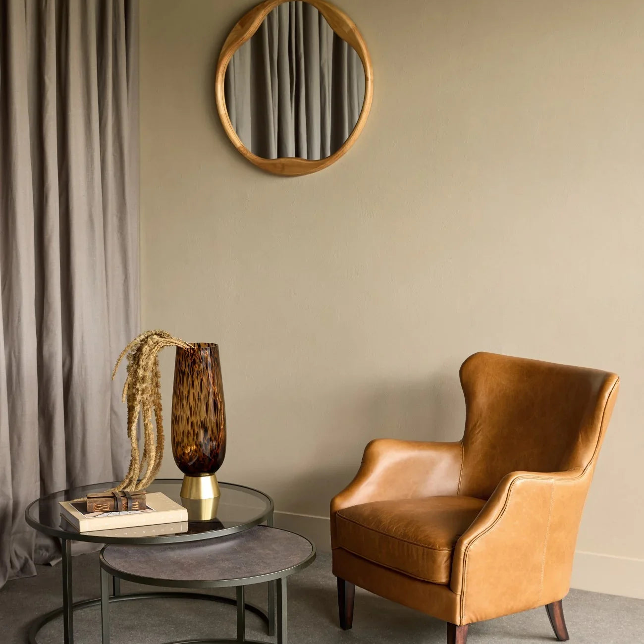 Nesting tables with glass and wood tops beside tan leather chair in cozy room.