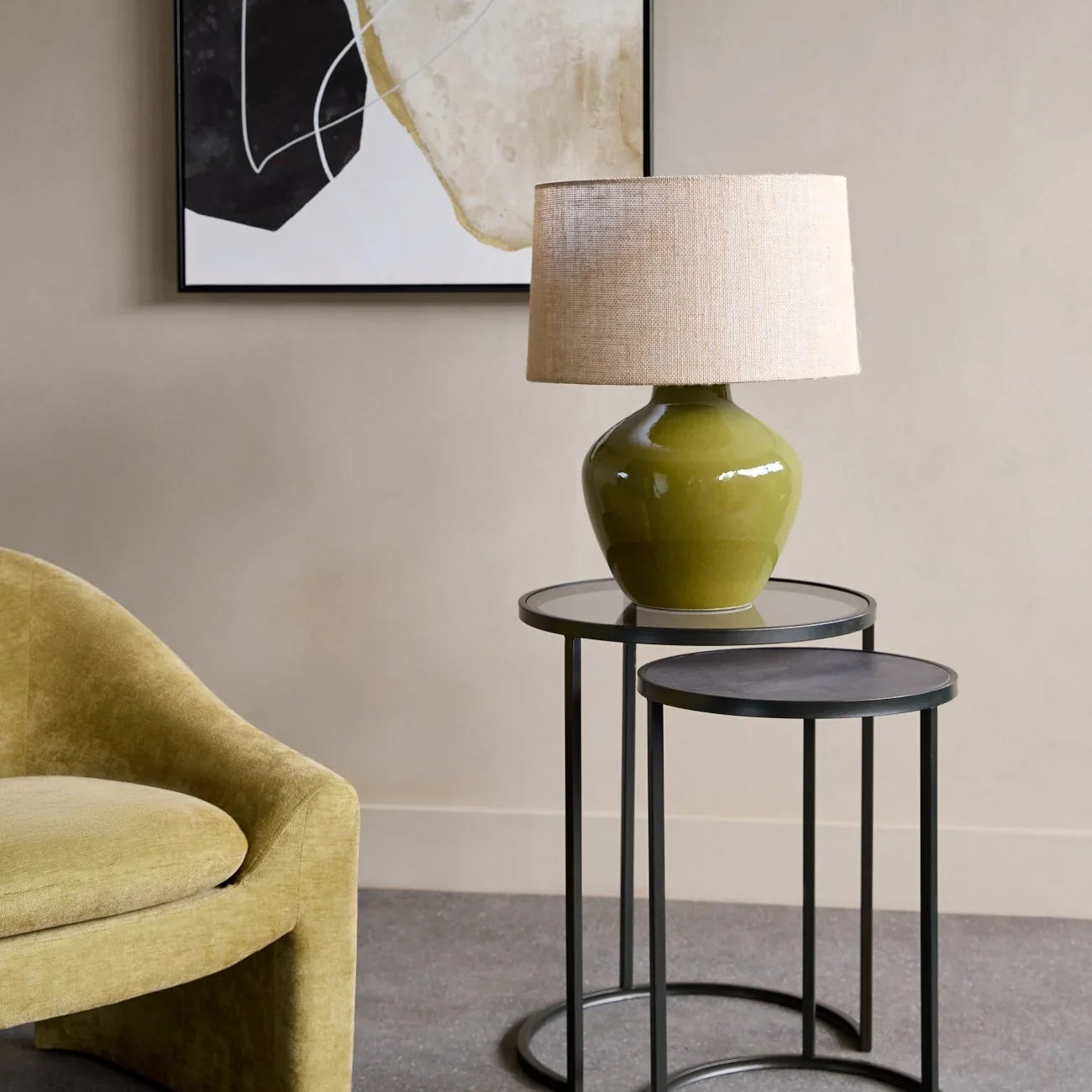 Black metal nesting tables with a green lamp, beside a yellow chair.