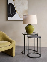 Black metal nesting tables with a green lamp, beside a yellow chair.