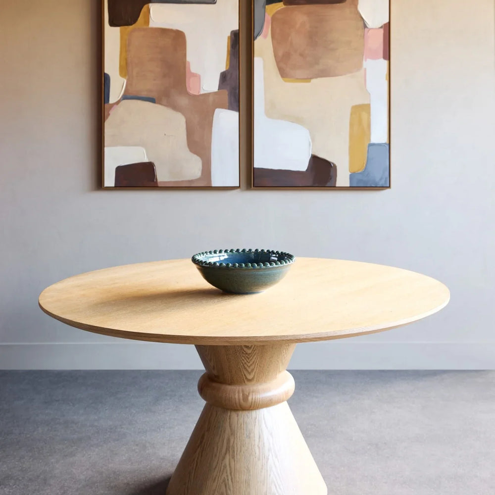 Round wooden dining table with pedestal base in modern room setting.