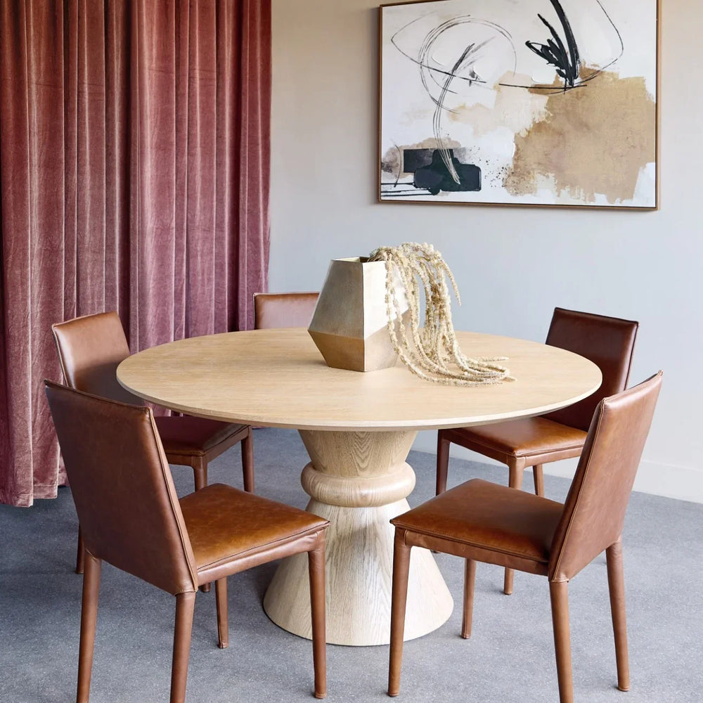 Round wooden dining table with pedestal base in elegant dining room setting.